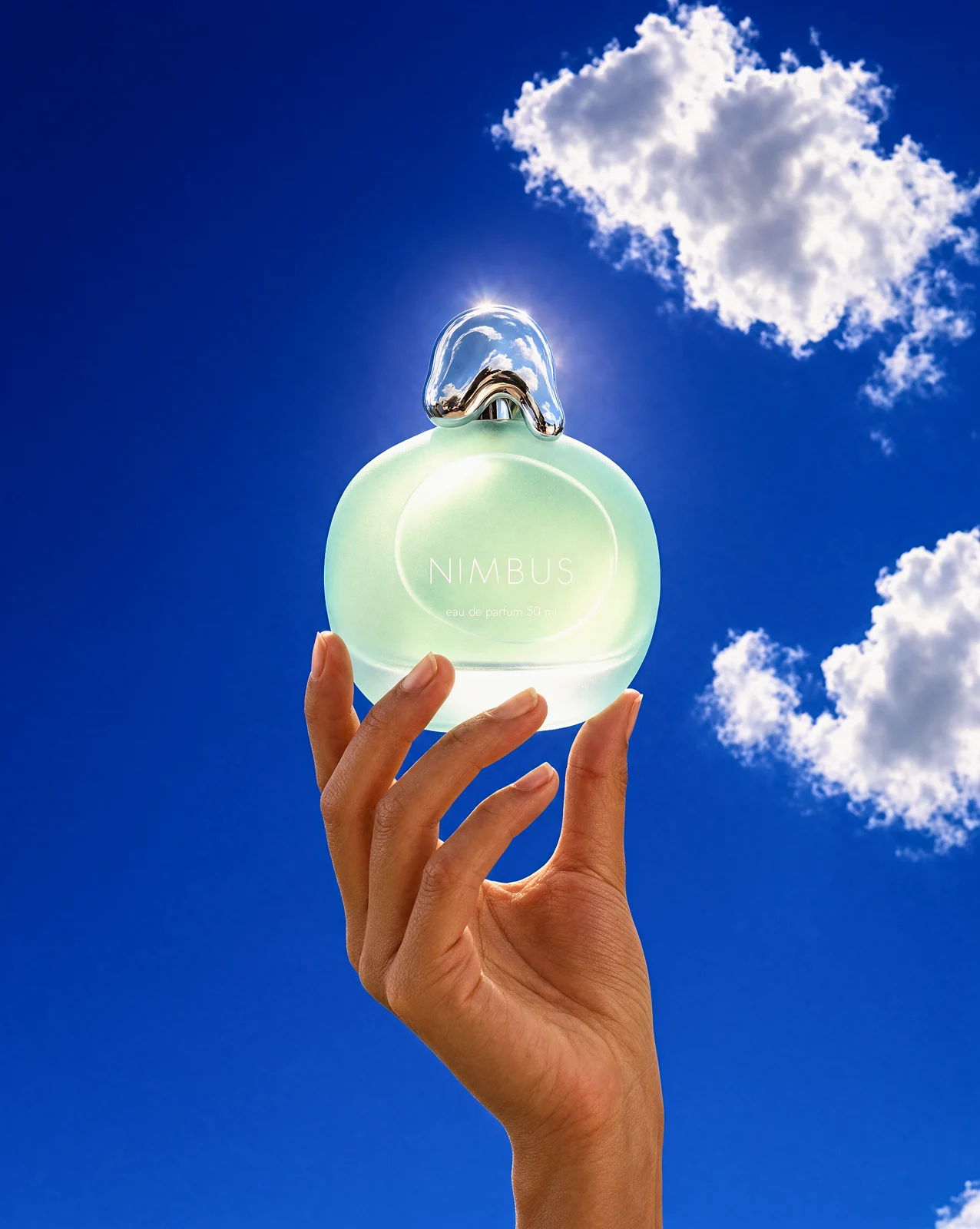 The same perfume bottle held up to a cobalt sky with clouds
