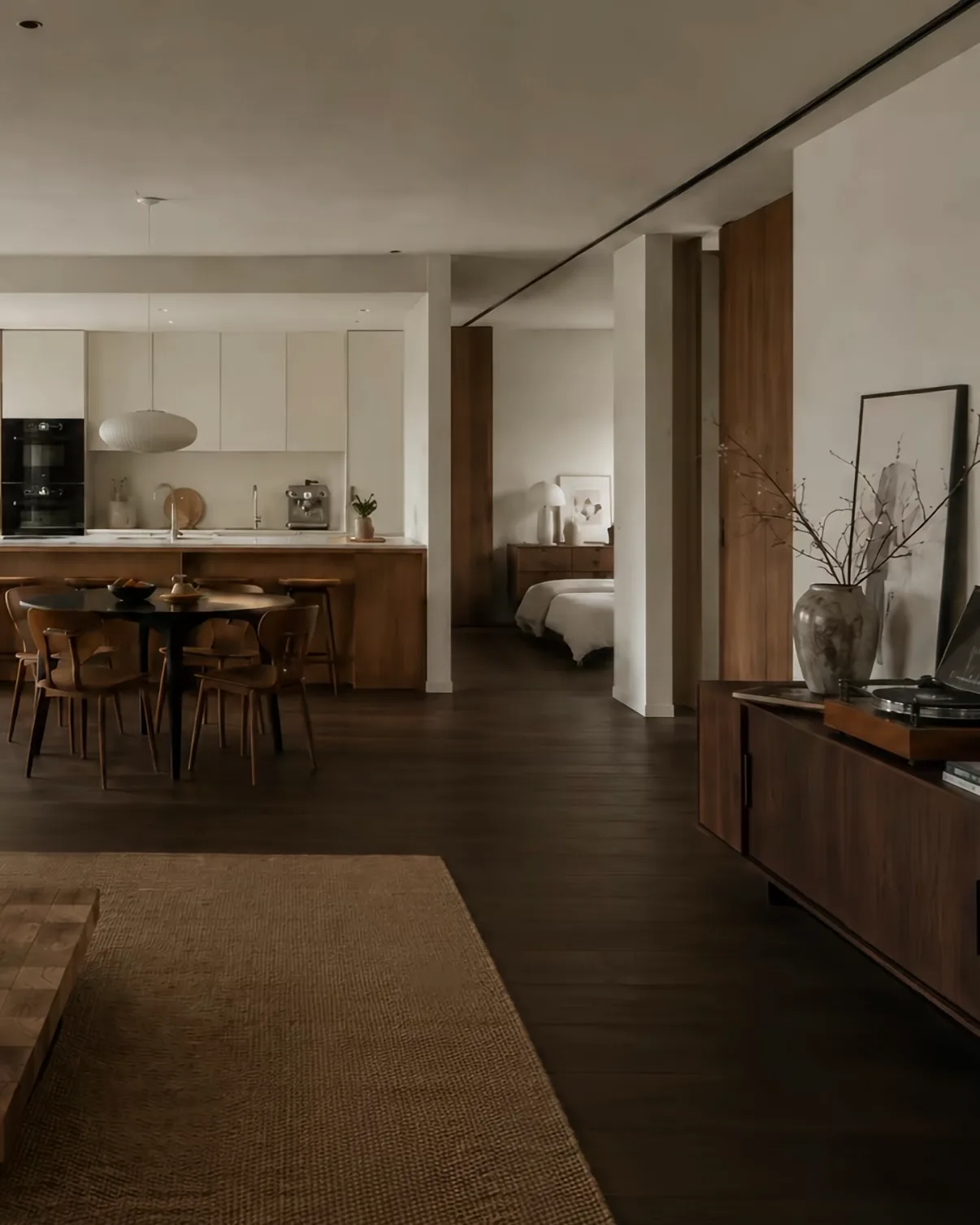 An open-plan apartment with dark timber floors, a walnut kitchen and warm white walls, seen from the living area.