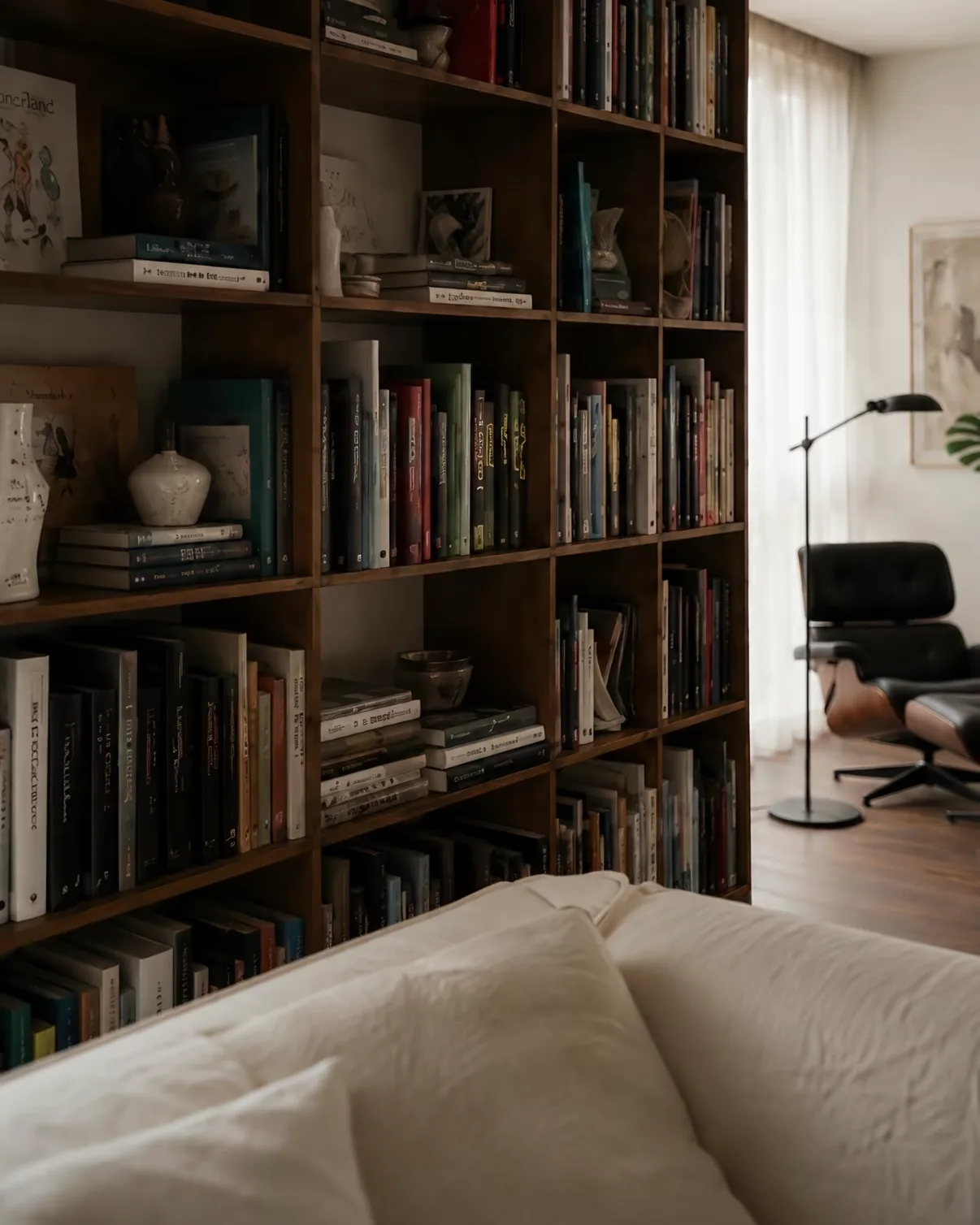 A full-height dark timber bookcase filled with books, with a white linen sofa in the foreground.