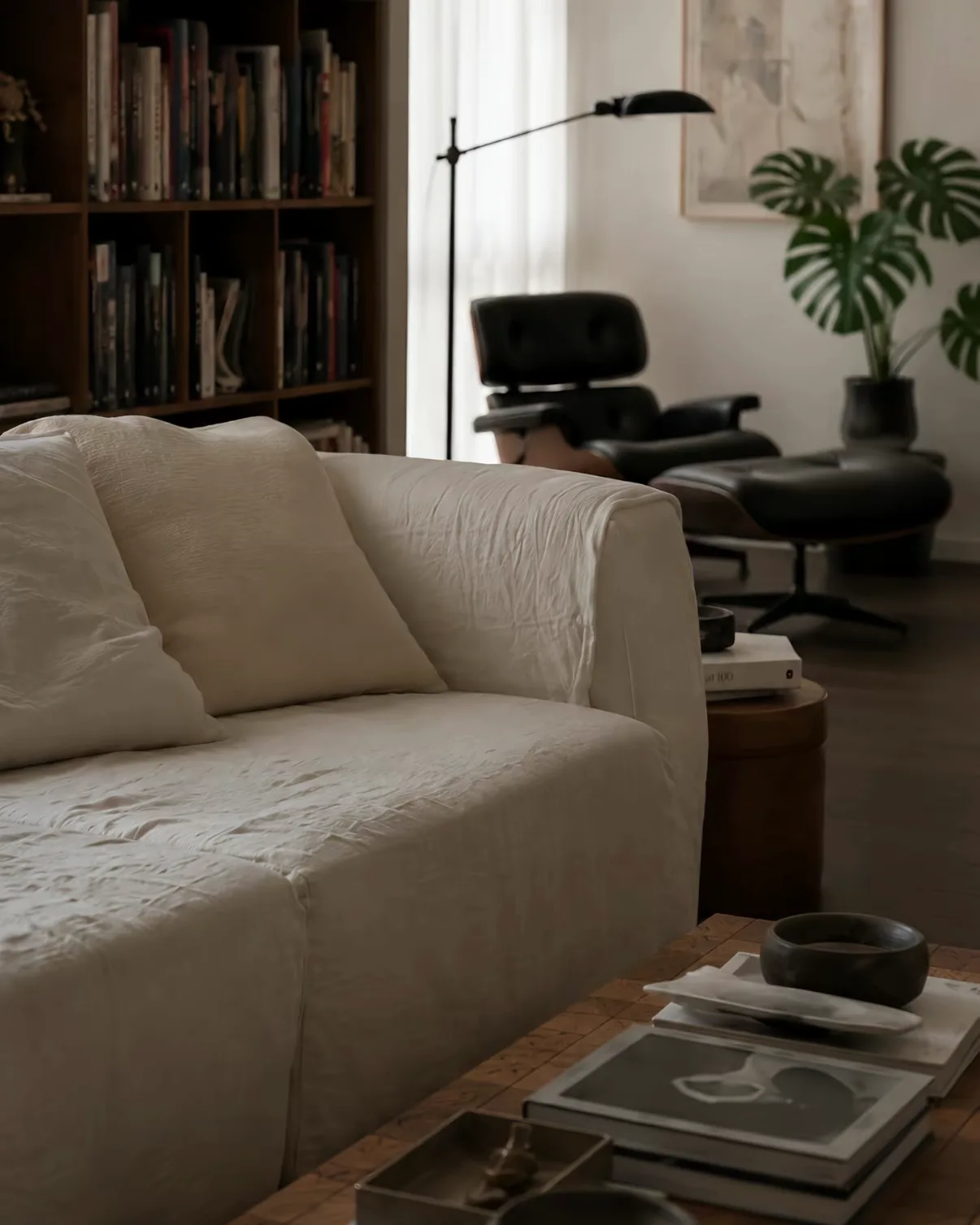 A rumpled white linen sofa with soft cushions, backed by a dark bookcase.