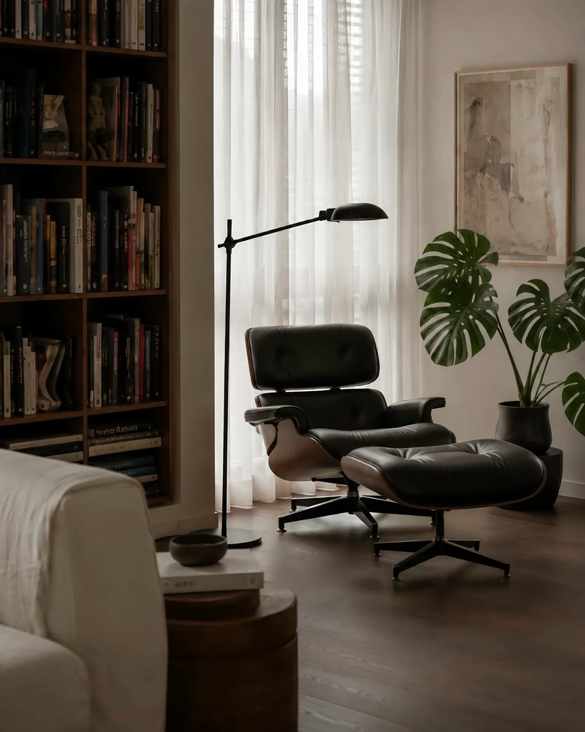 A leather lounge chair beside a sheer-curtained window, with light falling off into the darker room behind.