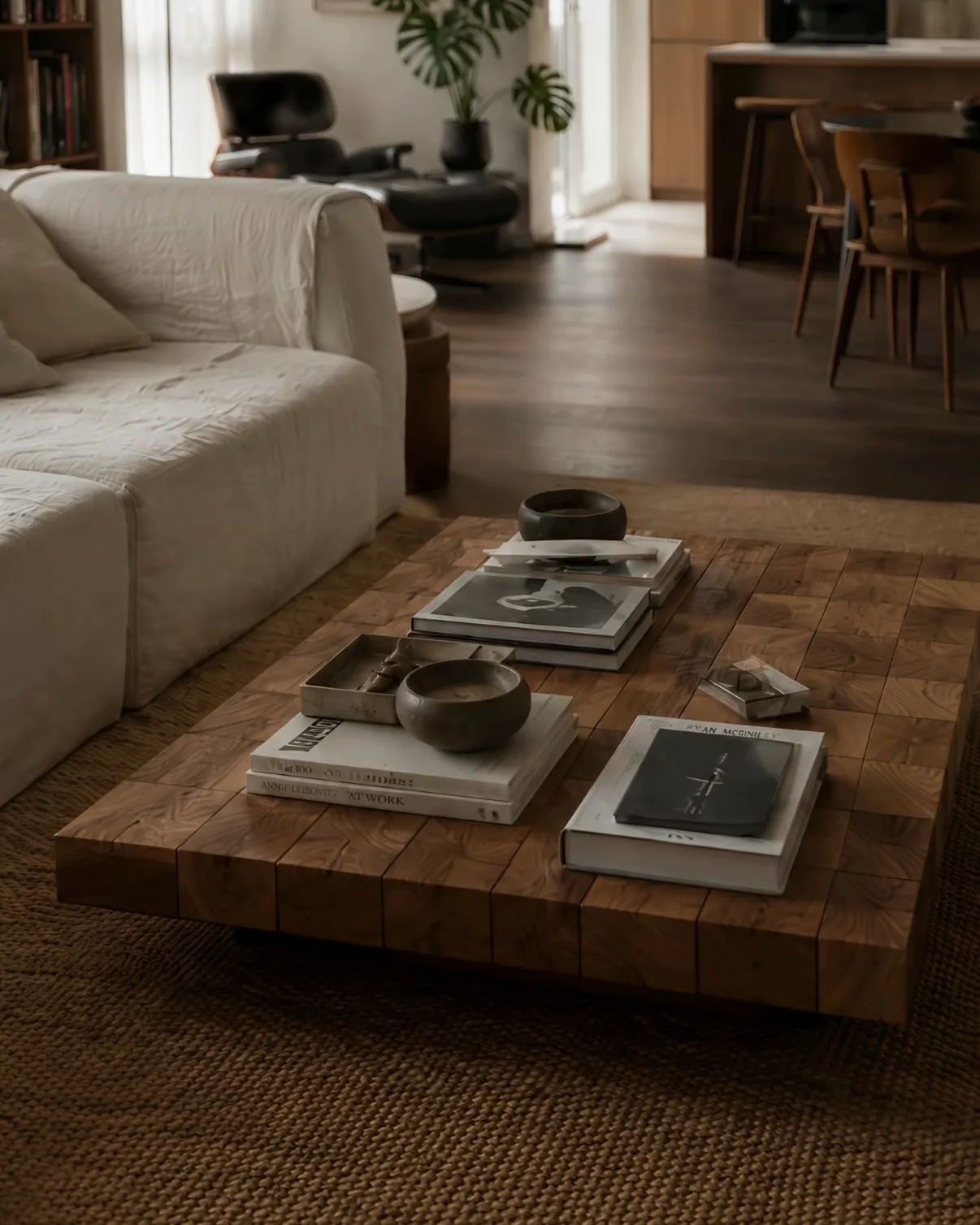 A low timber block coffee table holding stacked books, a dark wooden bowl and a small tray.