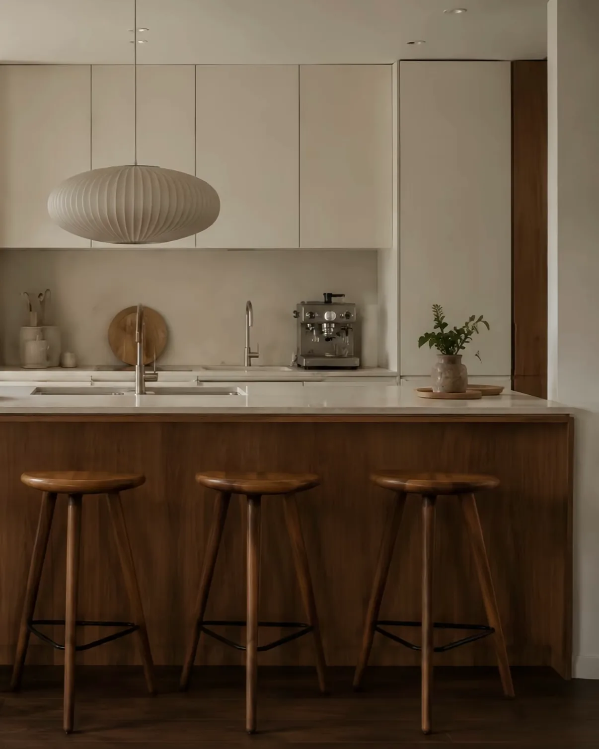 A kitchen with pale flat-fronted cabinets above a walnut island and three wooden stools.