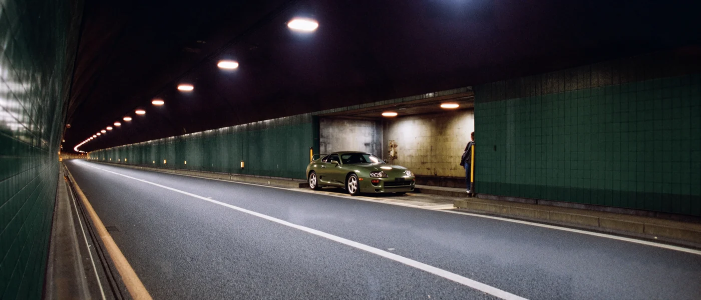 Car driving through a lit green tunnel at night