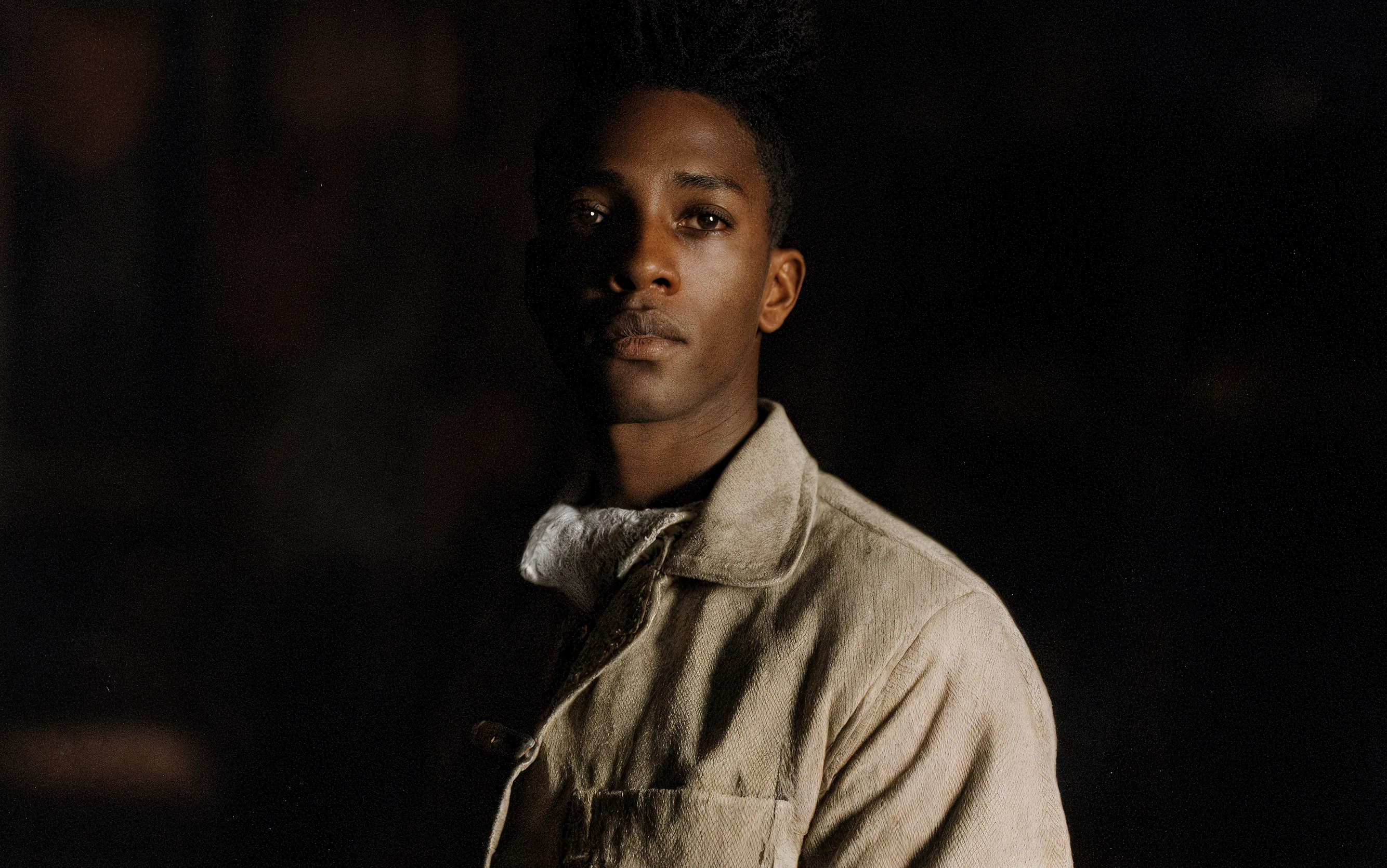 A man wearing old school clothes, cinematic portraiture, moody tonal contrast, soft lighting, subdued color grading, chiaroscuro influence, soft directional light, textural realism, vintage sartorial aesthetic, editorial photography, tactile fabric detail, mid-century color palette, analog depth.