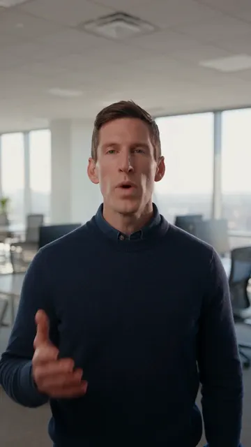 A man in a navy sweater talking to camera in an office