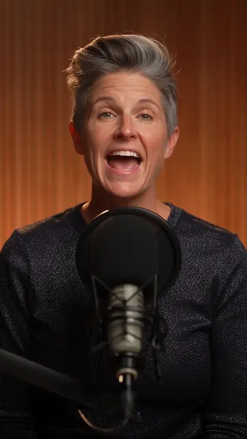 A woman with grey hair talking at a podcast microphone