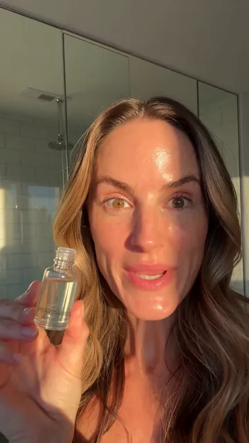 A woman holding up a serum bottle in a selfie video