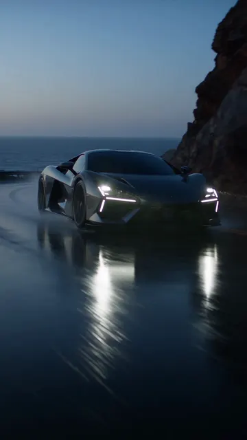 A black sports car on a wet coastal highway at dusk