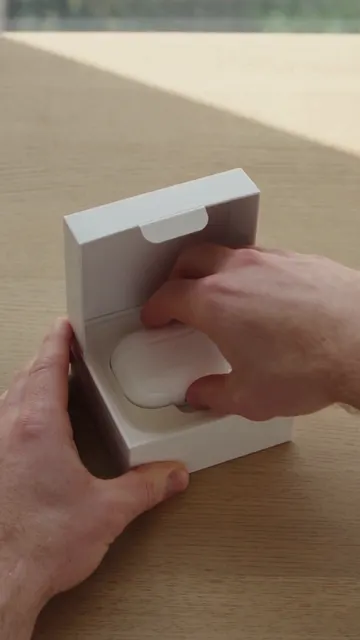 Hands unboxing white wireless earbuds on an oak desk